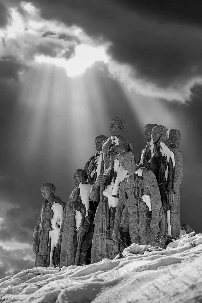 Les Fantômes de Landowski © Norbert Bardin Photo en noir et blanc de Norbert Bardin de la série "Commémoration du Centenaire de l’armistice de la grande guerre" de la sculpture Les fantômes de Landowski couverte de neige. Des raies de lumière percent les nuages semblant éclairer les soldats sculptés dans la roche.